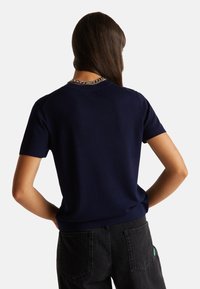 Námořnický pletený svetr s krátkým rukávem a kulatým výstřihem, s žebrovaným lemem. Hladká textura a střih přiléhající k tělu, v kombinaci s černými džínami s vysokým pasem.