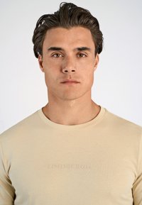 Beige pitkähihaisen t-paidan pyöreä pääntie ja kohokuvioitu 