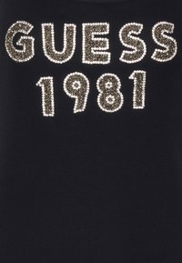 Tessuto nero con "GUESS 1981" scritto in strass dorati e bianchi.