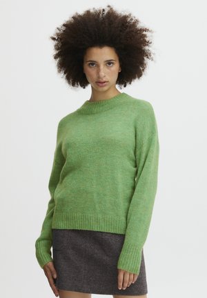 Grüner Wollpullover mit Rundhalsausschnitt, langen Ärmeln und gerippten Bündchen. Kombiniert mit einem dunkelgrauen Rock, der eine weiche, strukturierte Oberfläche hat.