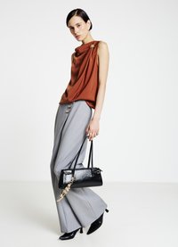 Rostfarbener ärmelloser Top mit Drapierung, graue, hochtaillierte Hose mit Knöpfen und eine schwarze Handtasche mit Kettenakzent. Schwarze spitze High Heels.