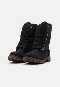 Bottes noires montantes avec un dessus texturé, un bout rond et une semelle robuste. Comprennent des lacets noirs épais et des œillets argentés pour le fermeture.