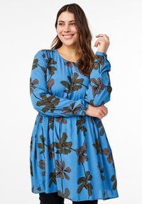 Blå blommig klänning med långa ärmar, prydd med stora bruna och svarta blommönster, samt en lös passform med rynk vid midjan.