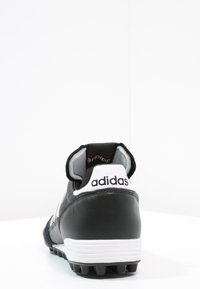 Botín de fútbol de cuero negro con un acento blanco en el talón, que cuenta con una suela texturizada para tracción y el logo de Adidas en la parte trasera.