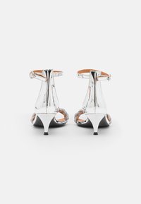 Srebrne sandały na wysokim obcasie z paskami wokół kostki, odkrytymi palcami i szpiczastym obcasem o gładkim, odbijającym światło wykończeniu oraz subtelnymi akcentami ze sprzętu.
