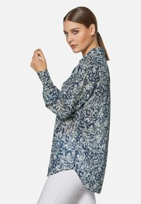 Bluse in Marineblau mit Blumenmuster, langen Ärmeln, kragenförmigem Ausschnitt und abgerundetem Saum. Leichter Stoff mit glatter Textur.