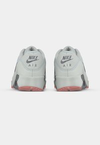 Ζευγάρι ανοιχτόγριων αθλητικών παπουτσιών Nike Air, που φαίνεται από πίσω, με κόκκινες λεπτομέρειες στη σόλα, πάνω σε λευκό φόντο.