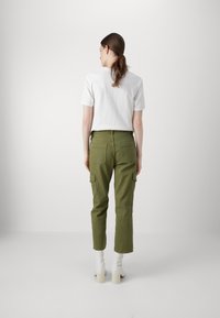 Groene cargo broek met zijzakken, taps toelopend ontwerp en stikseldetails. Gepaarde met een witte t-shirt met korte mouwen en witte haklaarzen.