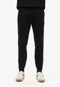 Zwarte joggers met een getailleerde pasvorm, uitgerust met twee zijzakken en een rood logodetail, gecombineerd met witte sneakers.