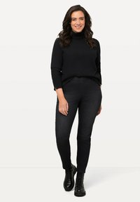 Suéter negro de cuello alto y jeans oscuros combinados con botas negras con cordones. El conjunto presenta un diseño relajado con un acabado de punto texturizado.