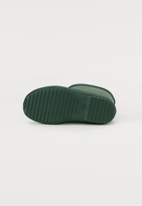 La semelle en caoutchouc verte présente une surface texturée avec un motif ondulé pour une meilleure adhérence. Le nom de la marque "HUNTER" est embossé au centre.