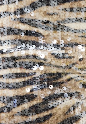 Beige stof dicht bedekt met glanzende zilveren pailletten, gerangschikt in onregelmatige zwarte en lichtbruine tijgerstreep patronen.