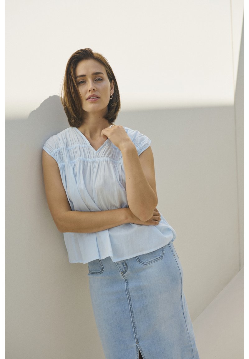 Haut texturé bleu clair à manches courtes avec des détails froncés, associé à une jupe midi en denim clair avec une fente à l'avant.
