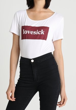 Weißes Baumwoll-T-Shirt mit burgunderfarbenem "lovesick"-Grafikdruck, Rundhalsausschnitt und kurzen Ärmeln, kombiniert mit hoch taillierter schwarzer Jeans.
