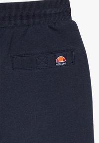 Temno modri bundi z mehkimi teksturami, z elastičnim pasom in majhnim vezenim ellesse logotipom na zadnjem žepu.