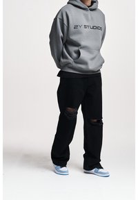 Grey hoodie with “2Y STUDIOS” text, front kangaroo pocket, paired with black ripped jeans and blue sneakers. Simple, relaxed fit design.