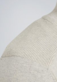 Beige Strickpullover mit Rippstruktur an den Schultern und weichem Finish. Der Stoff ist leicht und hat einen glatten, dezente Schimmer.