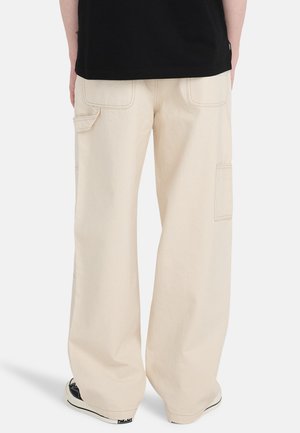 Beige cargobukser med løs pasform, lavet af slidstærkt stof. Har flere lommer og synlige syningsdetaljer. Sorte sneakers i bunden.