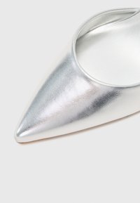 Sömlös silvermetallisk sko med spetsig tå i ett slätt lädermaterial och öppen häl. Viser en elegant design med minimalistiska detaljer.