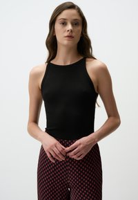 Zwarte geribbelde tanktop met een hoge hals, gecombineerd met gestreepte rode en zwarte legging met een diamantdesign. Soepele textuur, aansluitende stijl.