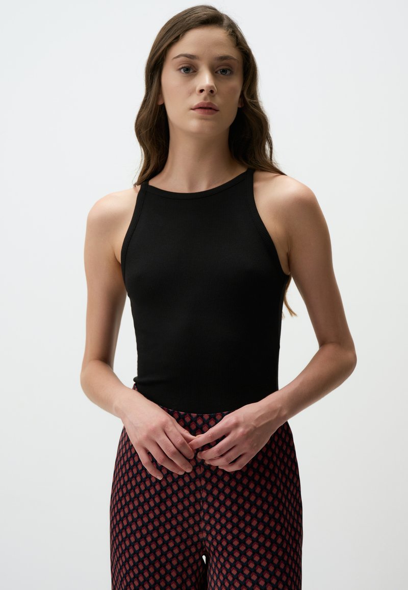 Zwarte geribbelde tanktop met een hoge hals, gecombineerd met gestreepte rode en zwarte legging met een diamantdesign. Soepele textuur, aansluitende stijl.