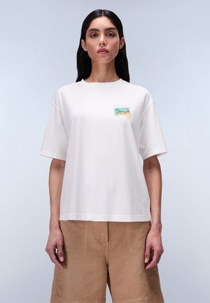 Tricou alb din bumbac, cu mâneci scurte și guler rotund. Are un imprimeu colorat în zona stângă a pieptului. Croială relaxată.