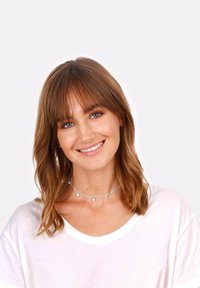 Collana choker in argento con piccole perline rotonde, indossata sopra una camicia bianca. Il modello ha capelli castano medio e un trucco naturale.