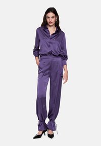 Purple satin matching set featuring a button-up shirt and drawstring pants, adorned with subtle floral embroidery and finished with tapered cuffs.