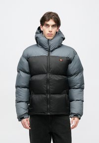 Prešívaná bunda s dvojfarebným dizajnom, vrchnou časťou v sivej farbe a spodnou v čiernej, vysokým golierom, celým zipsom a logom značky na hrudi.