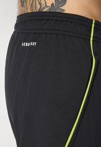 Zwarte sportieve shorts gemaakt van een lichtgewicht materiaal, met heldergroene zijaccenten en een elastische tailleband met logo.