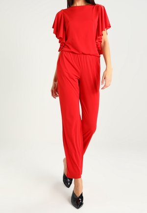 Czerwony kombinezon z falbaniastymi rękawami, elastycznym pasem i szerokimi nogawkami. Połączony z czarnymi szpilkami o spiczastym nosku. Gładki, rozciągliwy materiał.