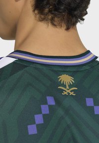 Green sports jersey with a textured pattern, featuring a gold palm and crossed swords logo on the back, and purple and gold striped collar.