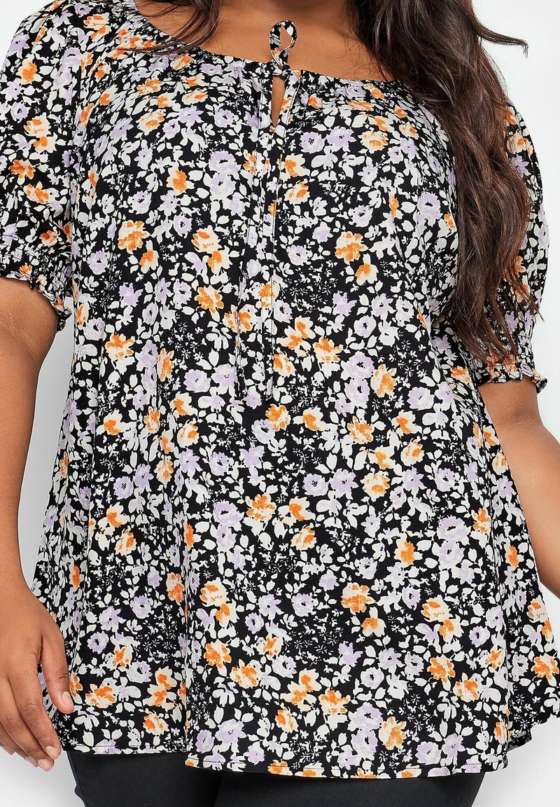 Top floral noir avec des fleurs lavande, orange et blanches ; présente un col froncé, des manches courtes bouffantes et un décolleté en forme de clé à l'avant.