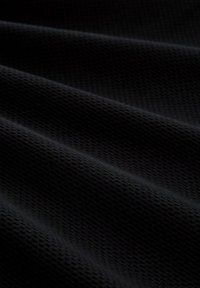 Detail tmavej látky s jemným textúrovaným vzorom a mäkkými záhybmi vytvárajúcimi jemné tiene na povrchu.