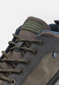 Tmavě šedé tenisky s texturovaným povrchem, zelenými akcenty, hexagonálními očky a gumovou podrážkou, s polstrovaným jazykem pro pohodlí.