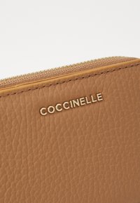 Brązowy skórzany portfel o teksturowanym wykończeniu, z złotym zamkiem błyskawicznym i wytłoczonym na złoto logo marki "Coccinelle".