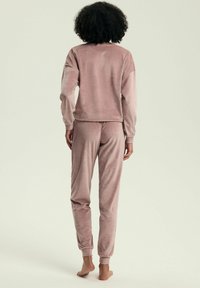 Różowy dres z weluru, składający się z bluzki z długim rękawem i zwężanych spodni. Gładka tekstura z elastycznymi mankietami i pasem w talii dla większego komfortu.