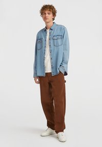 Light blue denim shirt with two chest pockets worn over a white T-shirt, paired with brown corduroy pants and white sneakers.