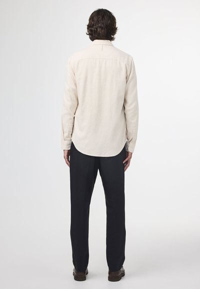 Beige langærmet skjorte med tekstureret finish, rygpanel og rundet kant, parret med sorte bukser og brune fodtøjer.