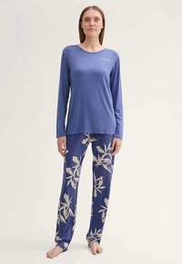 Hosszú ujjú kék felső kerek nyakkal; virágmintás pizsama nadrág tengerészkék és krém színekben. Puha anyag, laza szabás, teljes hosszúságú nadrág.