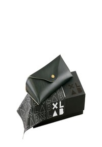 Portafoglio in pelle nera con chiusura dorata, appoggiato su una scatola nera con motivi geometrici bianchi e un tessuto con design coordinato.