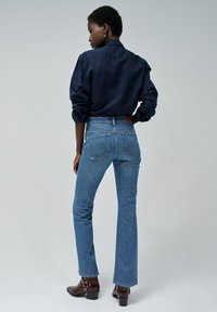 Džínové kalhoty s vysokým pasem v modré barvě, rovného střihu, se zesvětlenou texturou a dvěma zadními kapsami. Nosené s tmavým tričkem s dlouhými rukávy a botami.