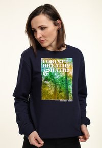 Felpa blu navy con grafica quadrata di alberi e il testo "FOREST BREATHE & BATH," in un gradiente di colore sovrapposto che va dal verde al giallo.