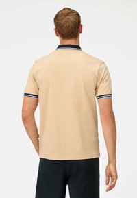 Beige polo shirt met een klassieke kraag met marineblauwe en witte strepen, korte mouwen met vergelijkbare gestreepte accenten en een zachte textuur.