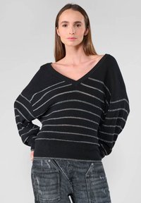 Zwarte gebreide sweater met zilveren horizontale strepen, V-hals en oversized mouwen. Textiel met een structuur, ontspannen pasvorm, gecombineerd met donkere jeans.