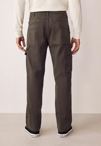 Cargo-Hosen in dunkelolivgrün mit geradem Bein, mehreren Taschen und einer robusten Stoffstruktur. Schwarze Sneakers getragen.