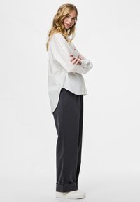 Camisa blanca de botones con mangas largas, de corte relajado; combinada con pantalones de tiro alto en gris oscuro y zapatillas blancas. Diseño simple y moderno.