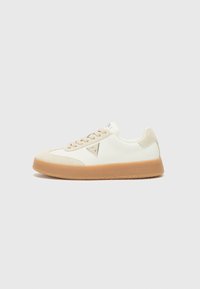 White sneaker with beige accents, suede and leather materials, rounded toe, rubber sole, and a triangular logo detail on the side.