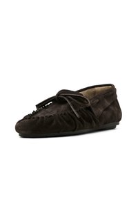 Mocassino scamosciato marrone scuro con punta arrotondata, dettagli in frange nella parte anteriore e un fiocco decorativo sulla tomaia. Suola piatta.