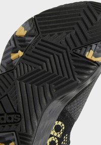 Black athletic shoe sole featuring textured rubber with zigzag and circular patterns. Accents of yellow near the heel. Durable material.